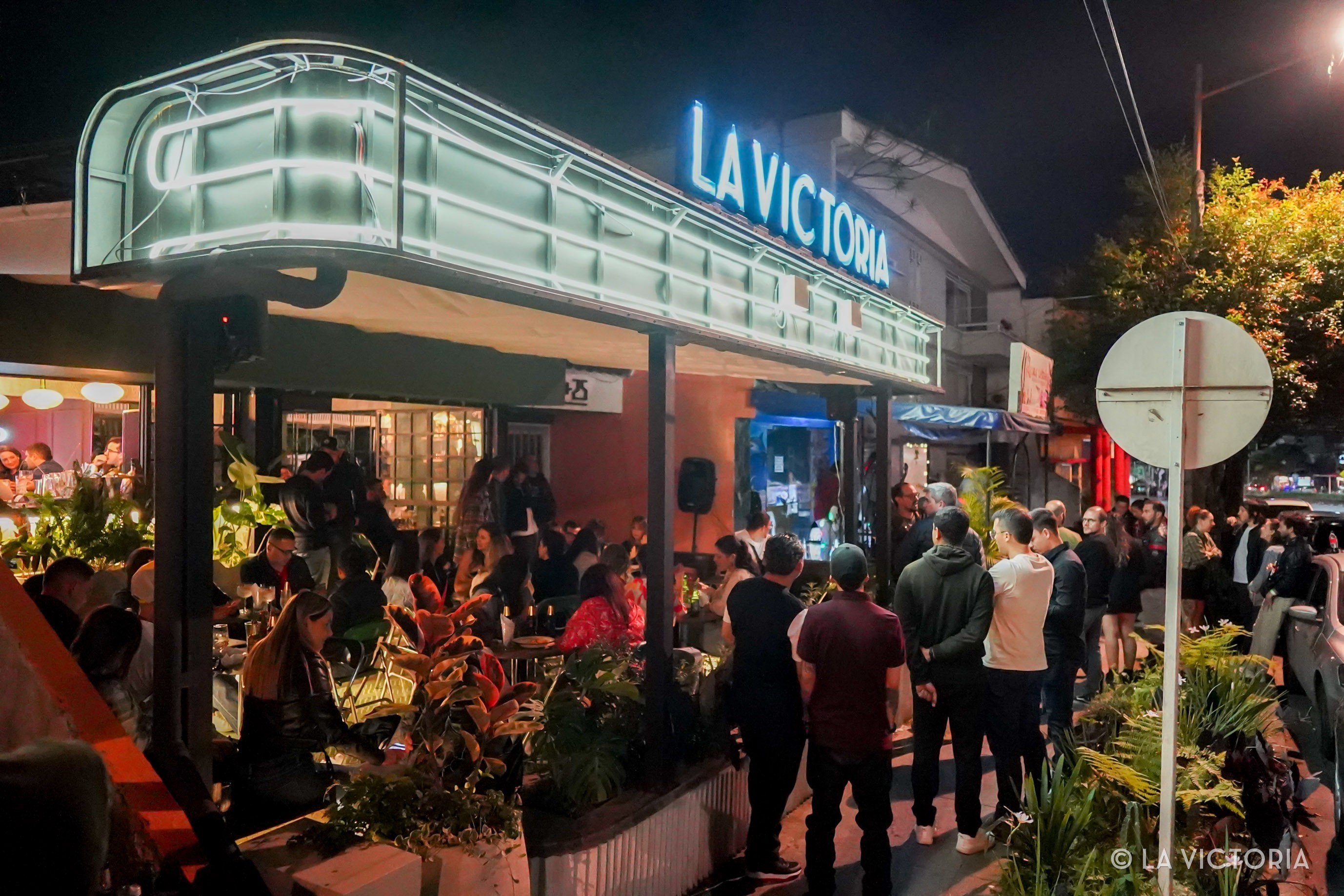 Fachada de La Victoria de noche con el letrero de neón y gente afuera